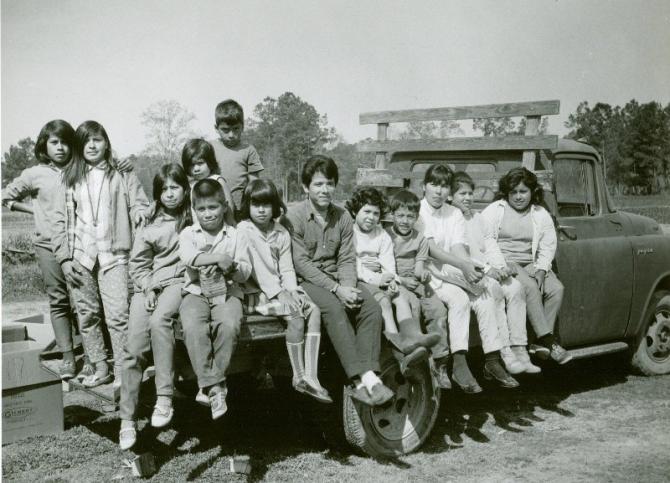 A black and white photo of migrant children sitting on a flatbed farm truck. It was likely taken in the 1960s.